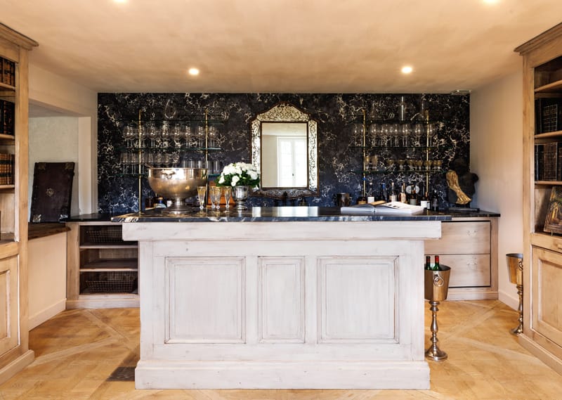 Chateau bar with black marble wall, gilt mirror, silver champagne bowl, white roses, and antique bookshelves