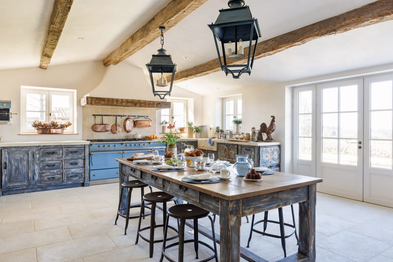 Rustic French kitchen with navy blue cabinetry, La Cornue range, wooden island set with croissants and tableware