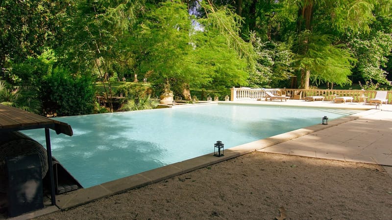 Rectangular swimming pool with stone balustrade wooden sun loungers and estate grounds