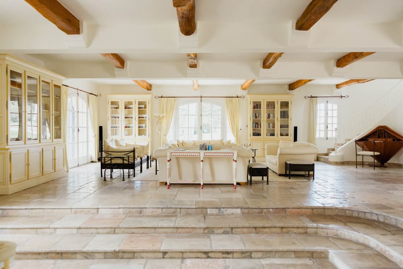 Light-filled salon with exposed beams cream sofas bookcases and arched French windows in Provencal country estate