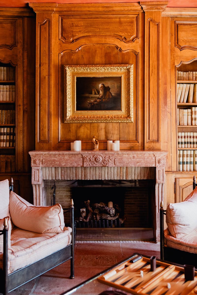 Honey-toned wood-panelled library with carved boiserie, stone fireplace, and antique leather-bound books