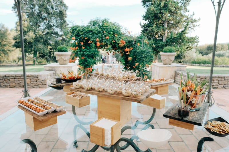 Canape station on wrought-iron table with tiered wood risers on stone terrace with formal garden beyond