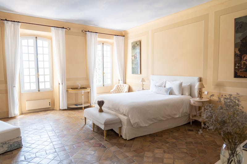 Chateau bedroom suite with white linens, arched French windows, terracotta tile floors, and gilt furnishings