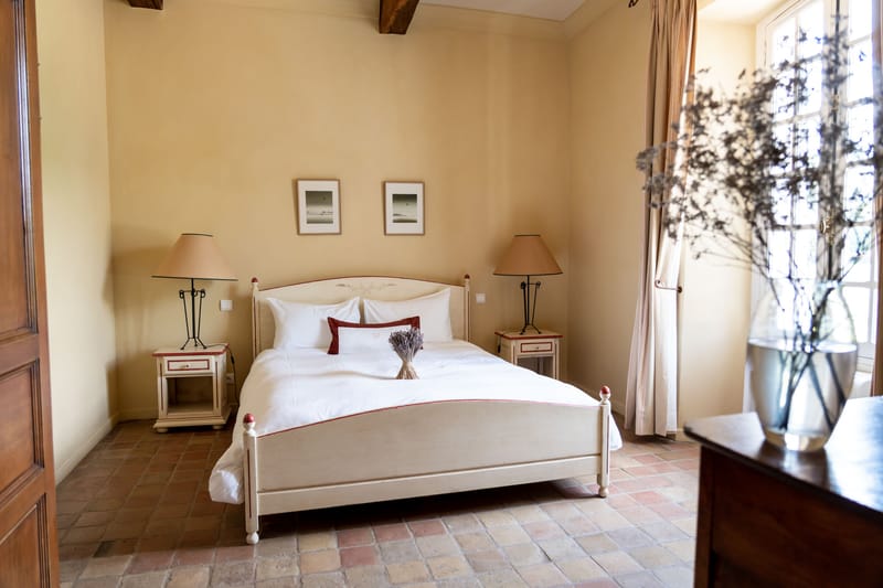 Provencal guest bedroom with cream bed frame, terracotta tile floor, exposed beams, and ochre walls