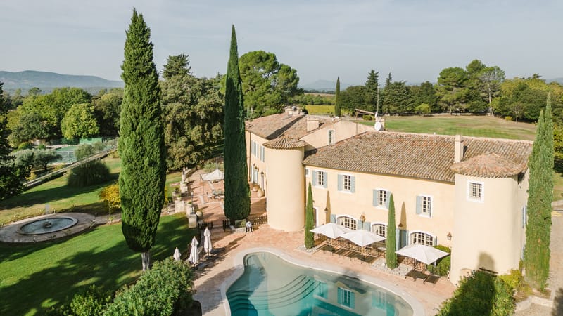 Aerial view of ochre Provencal bastide with freeform pool cypress trees and distant mountains