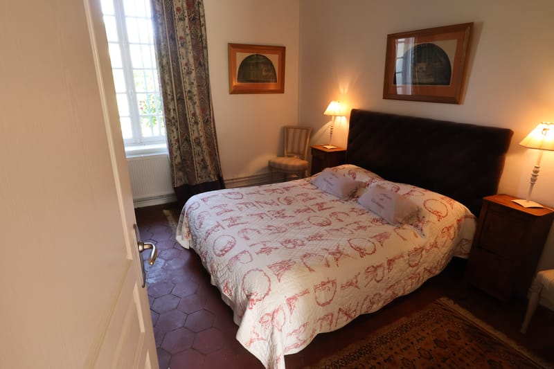 Guest bedroom in French manor with toile bedding, terracotta tile floors, and floral curtains
