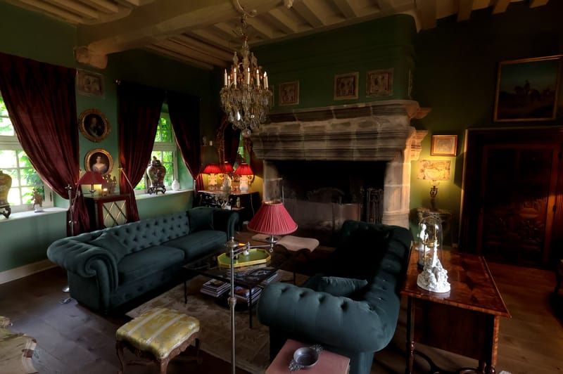 Chateau salon with forest-green walls, teal Chesterfield sofas, stone fireplace, and crystal chandelier