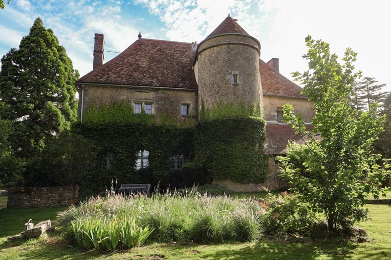 French chateau exterior with ivy-covered facade, round stone tower with terracotta roof, and garden beds