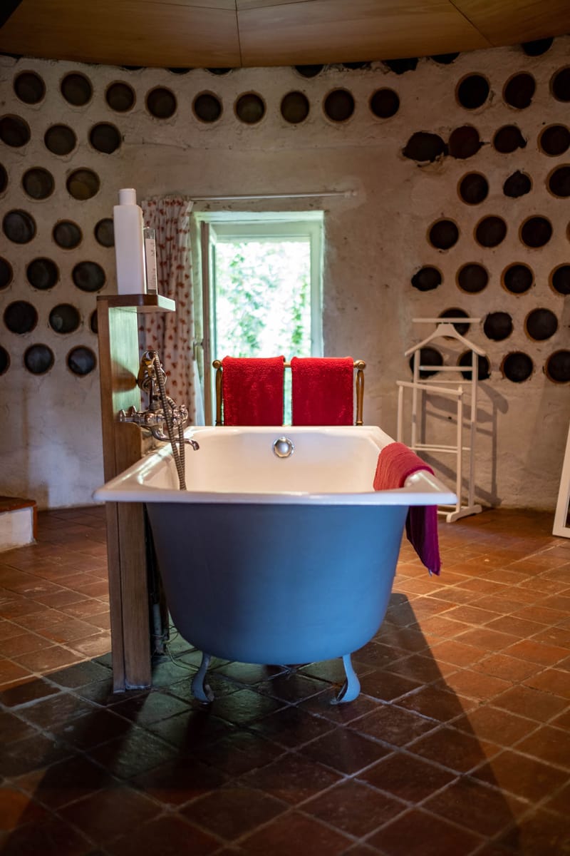 Freestanding pale blue clawfoot bathtub in rustic venue bathroom with bottle-end wall recesses and wooden beams