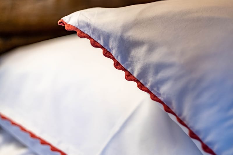 Close-up of white bed linens with terracotta red rickrack trim on pillowcase and sheet