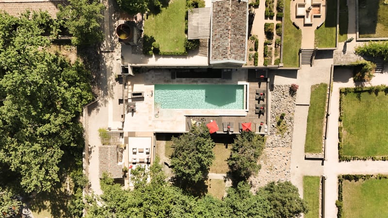 Aerial view of chateau grounds with turquoise infinity pool, sun loungers, covered terrace, and formal parterre garden