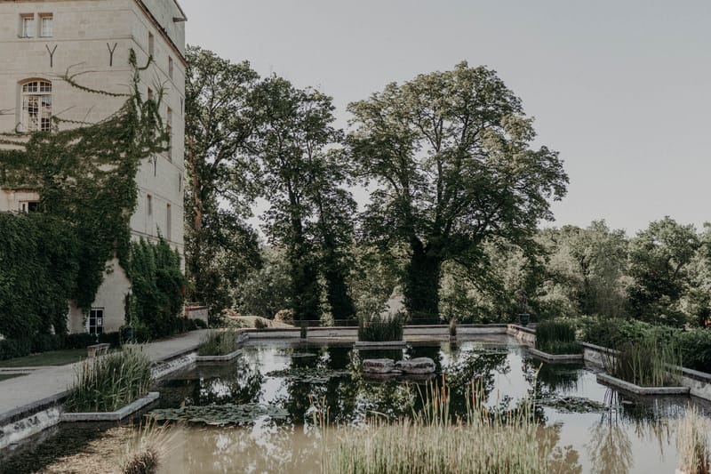 French chateau exterior with rectangular ornamental pond, lily pads, and ivy-covered limestone facade