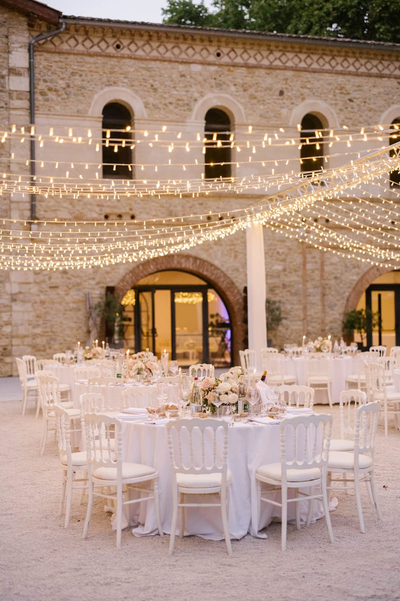 Courtyard reception with round tables under fairy light canopy at dusk with blush centerpieces