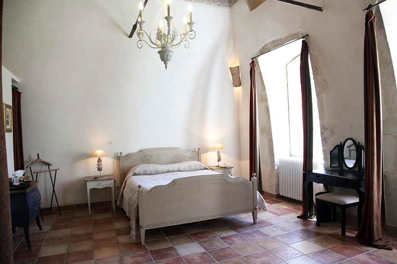 French provincial bedroom with carved bed, wrought-iron chandelier, terracotta tiles, and burgundy curtains