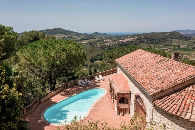 Aerial view of Provencal stone villa with oval pool on hillside terrace overlooking sea and valley