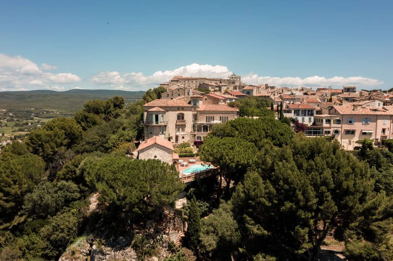 Aerial view of Provencal hilltop village with stone manor, chapel, pool, and round reception tables
