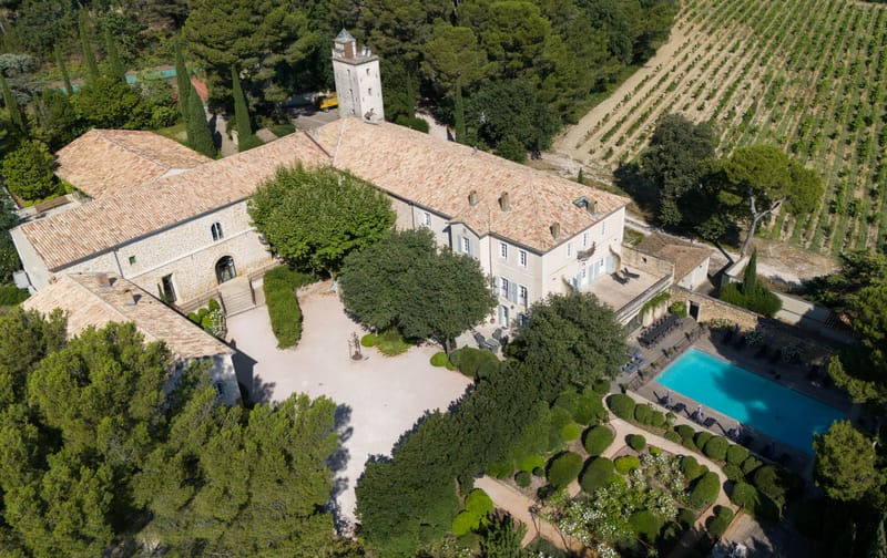 Aerial view of chateau estate with pool, formal gardens, vineyards, and cypress-lined perimeter