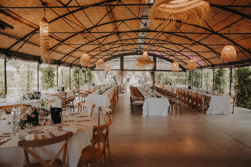 Boho reception venue with wicker pendant lights, round and banquet tables, and blush floral centerpieces