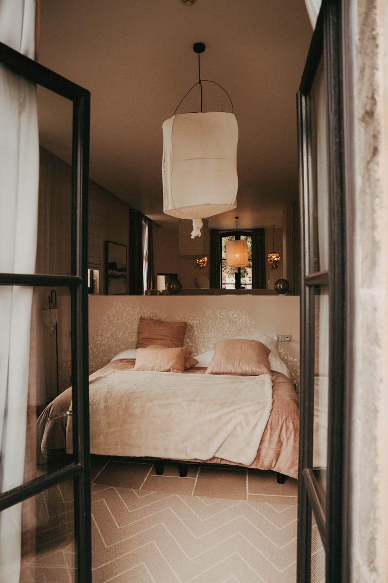 Venue bedroom with blush pink bedding and floral headboard viewed through open black-framed glass doors