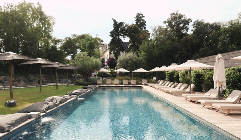 Chateau swimming pool with wooden sun loungers and parasols on deck terrace, main building in background