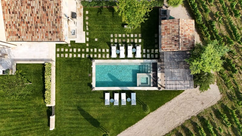 Aerial view of French country estate with turquoise swimming pool, sun loungers, and surrounding vineyards