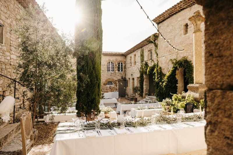 Outdoor reception tables with olive branch runners and taper candles in a stone courtyard with fairy lights