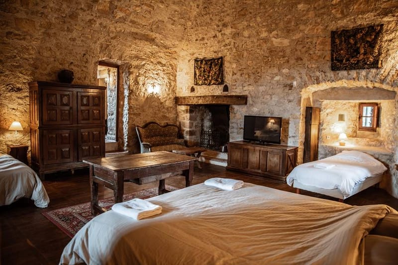 Stone-walled chateau guest room with vaulted ceiling, white-dressed beds, armoire, and fireplace