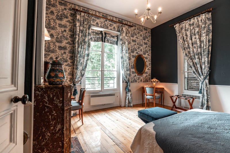 Chateau bedroom with navy toile de Jouy wallpaper, teal ottoman, and red marble fireplace