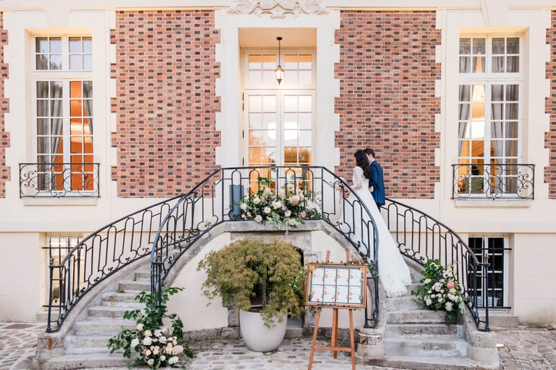 Couple at top of curved staircase with blush dahlia and hydrangea arrangements draped over iron railings