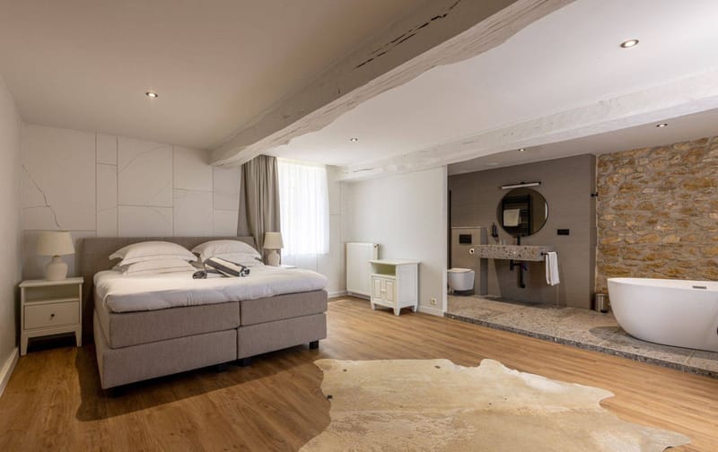 Hotel suite with king bed, cowhide rug, freestanding bathtub, and exposed stone wall in neutral tones