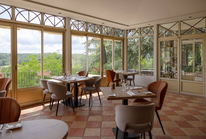 Conservatory dining room with arched windows, terracotta checkerboard floor, and velvet and leather chairs