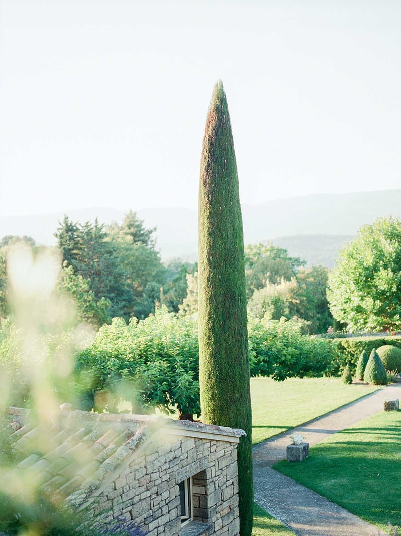 Provencal stone building with cypress tree and formal box hedges overlooking rolling hills