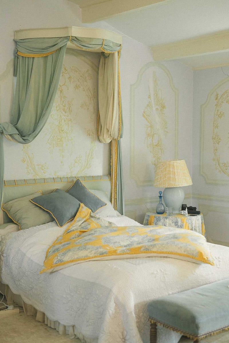 Elegantly decorated hotel bedroom with four-poster canopy bed in sage green, cream quilted bedding and toile floral wallpaper