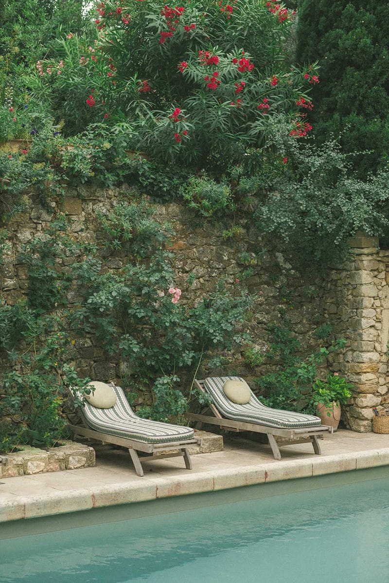 Poolside loungers with cream cushions on stone terrace beside turquoise pool and vine-covered stone walls