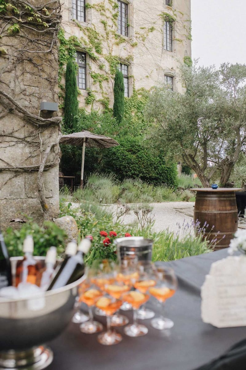 Cocktail hour setup with rose champagne and aperol spritz on a service table in an ivy-covered chateau courtyard