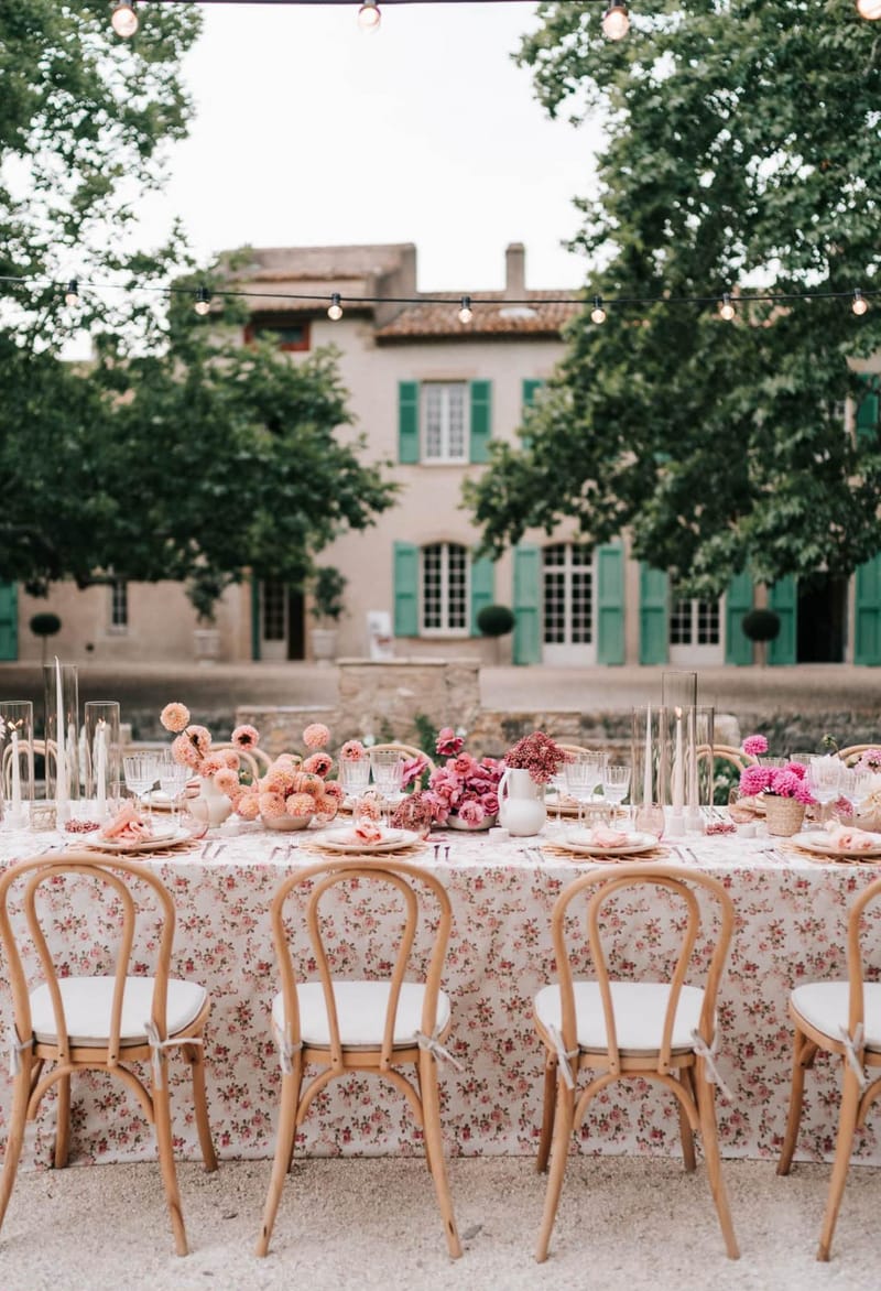 Outdoor reception table with peach dahlias and pink roses in white pitchers at French mas with teal shutters
