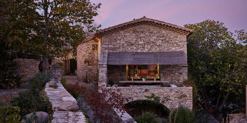 Provencal stone mas at dusk with warm interior lighting and string lights along garden pathway