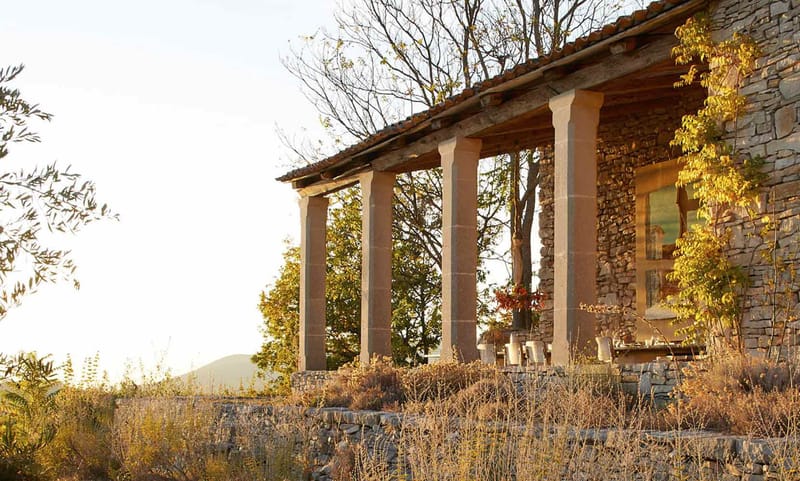 Rustic stone colonnade terrace with set dining table overlooking hillside at golden hour