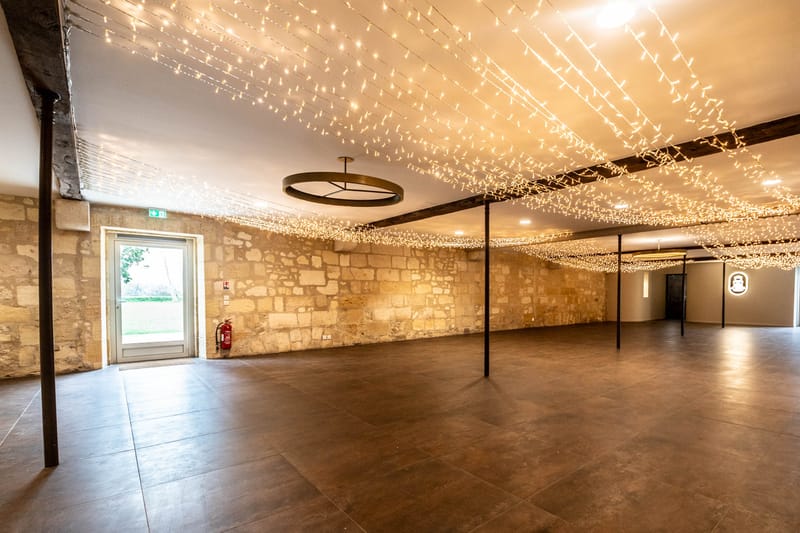 Converted stone barn reception hall with cascading fairy light ceiling, brass pendant, and dark tile floor