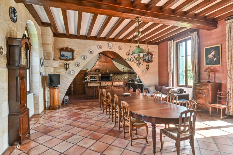 Rustic French dining room with beam ceiling oval table rush chairs grandfather clock and stone arch kitchen