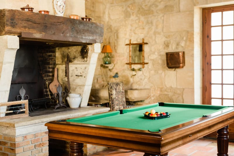 Rustic games room with billiard table stone walls open fireplace copper pots and tapestry chair