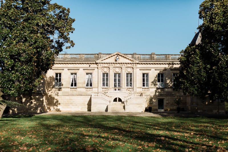 Classical 18th-century limestone chateau with carved pediment, balustrade roofline, and double staircase on lawn