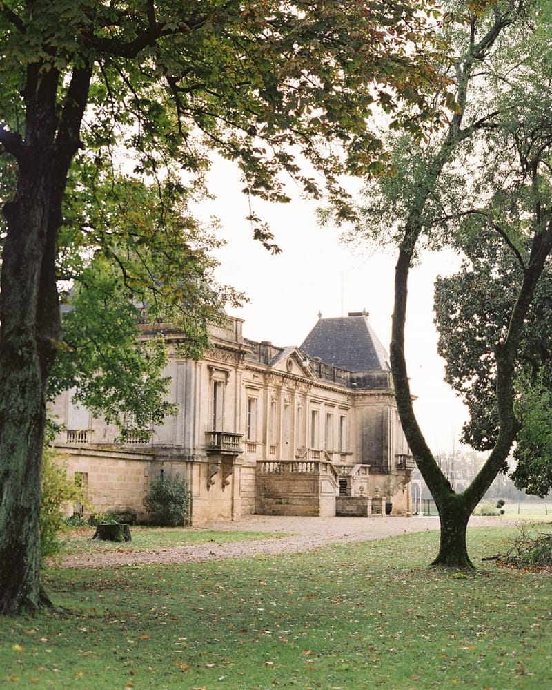 Classical limestone chateau with mansard roof stone balustrades and autumn lawn framed by trees