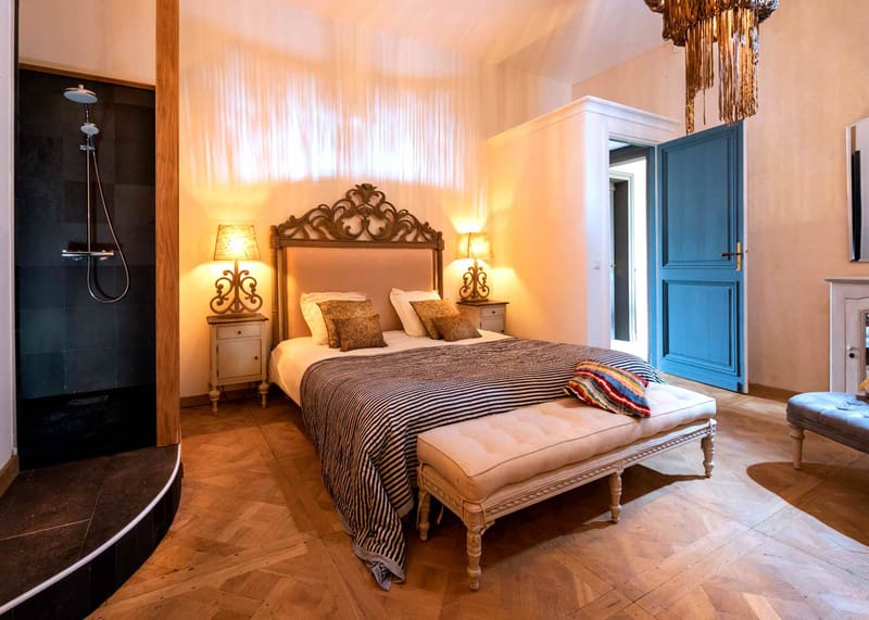 Chateau bedroom with carved headboard, gold chandelier, teal doors, and marble fireplace