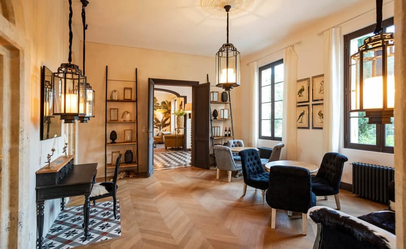 Interior of chateau reception room with herringbone floors, navy armchairs, lantern pendants, and eclectic decor