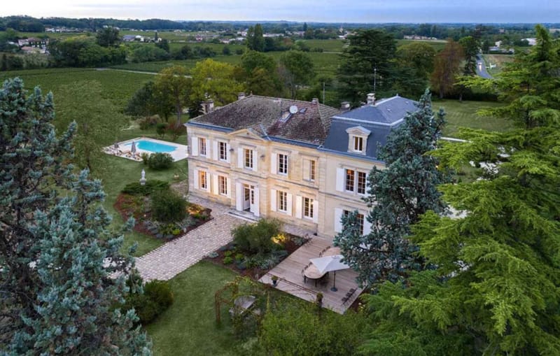 Aerial dusk view of Bordeaux chateau with slate mansard roof swimming pool vineyard and conifer trees