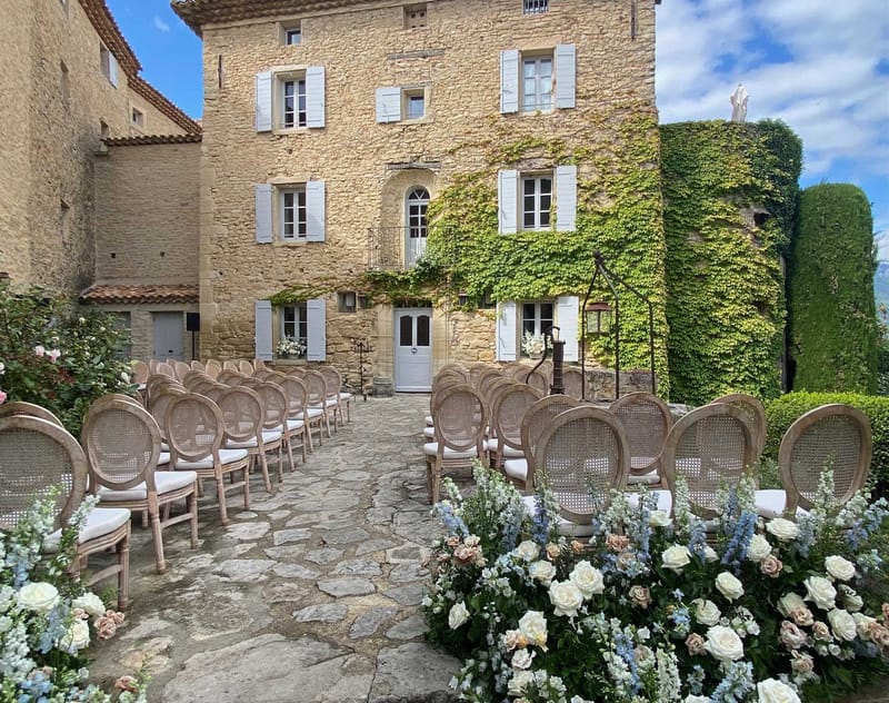 Outdoor ceremony setup with cane-back chairs and rose-lined aisle in an ivy-covered chateau courtyard