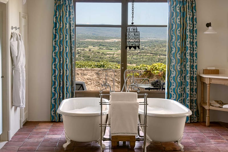 Chateau bathroom with twin clawfoot bathtubs, Moroccan lantern, and panoramic valley view through floor-to-ceiling window