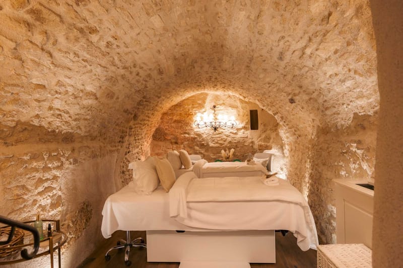 Vaulted stone spa room with two massage tables white linens wrought iron sconce and honey-toned walls