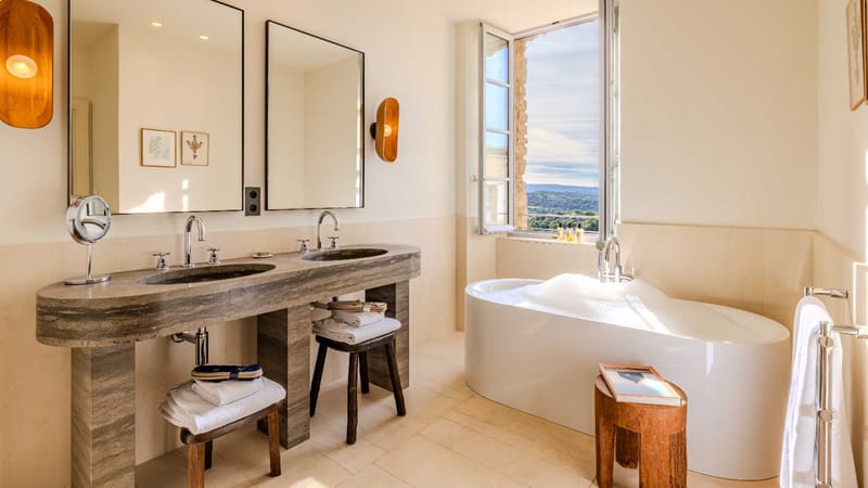 Venue bathroom with grey marble double vanity, freestanding bathtub beneath open window with countryside view